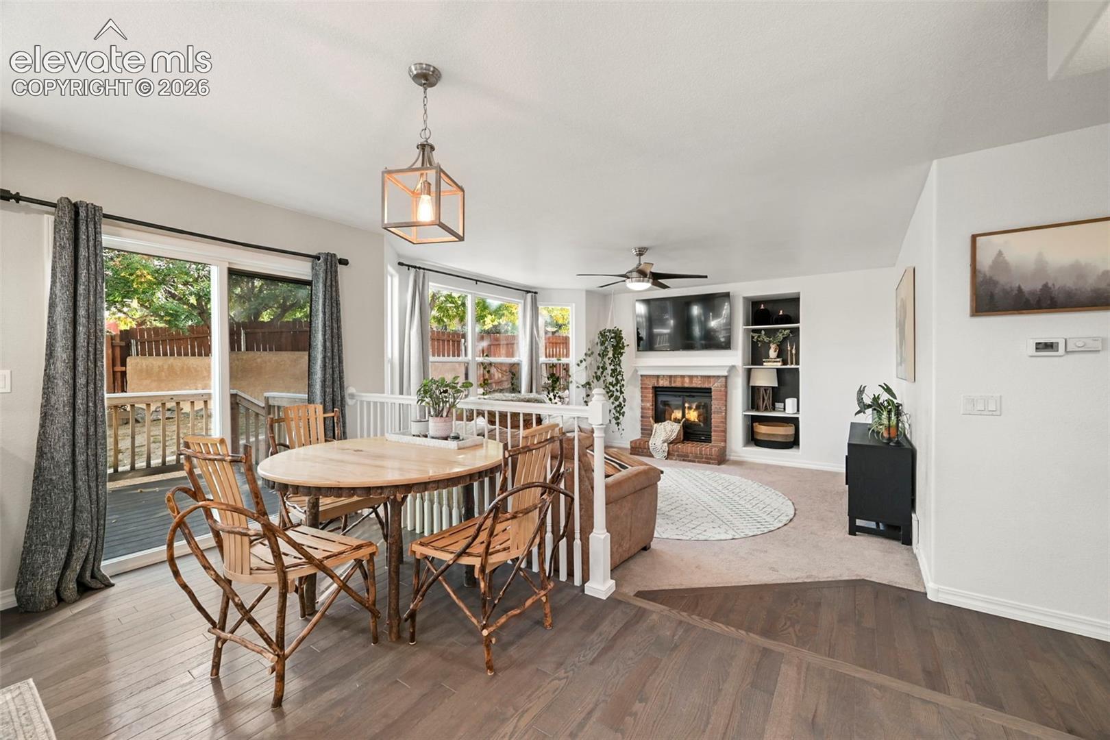 Hardwood-finish flooring, sliding glass door with deck access, brick-surround fireplace, built-in shelving, and ceiling fan