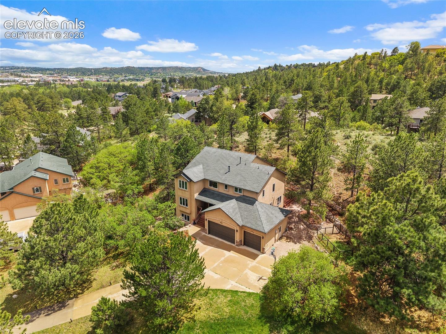 Multi-story exterior featuring a shingled roof, attached three-car garage, concrete driveway, and expansive lot with mature coniferous trees