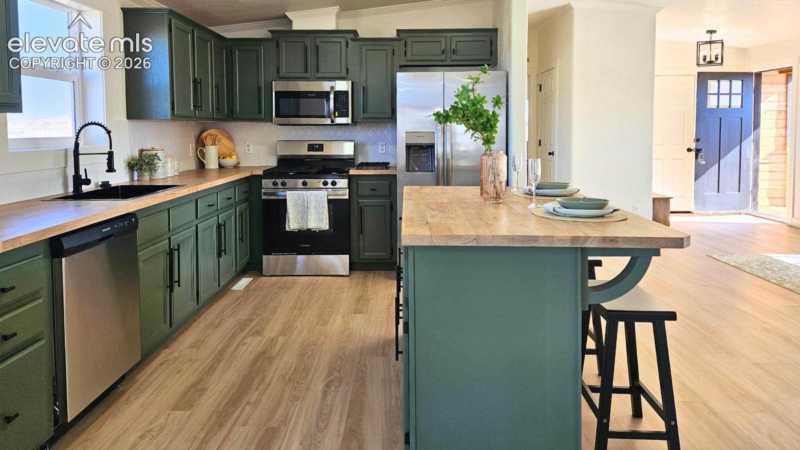 Kitchen featuring custom green cabinetry, butcher block countertops, stainless steel appliances, a center island, and wood-finish flooring