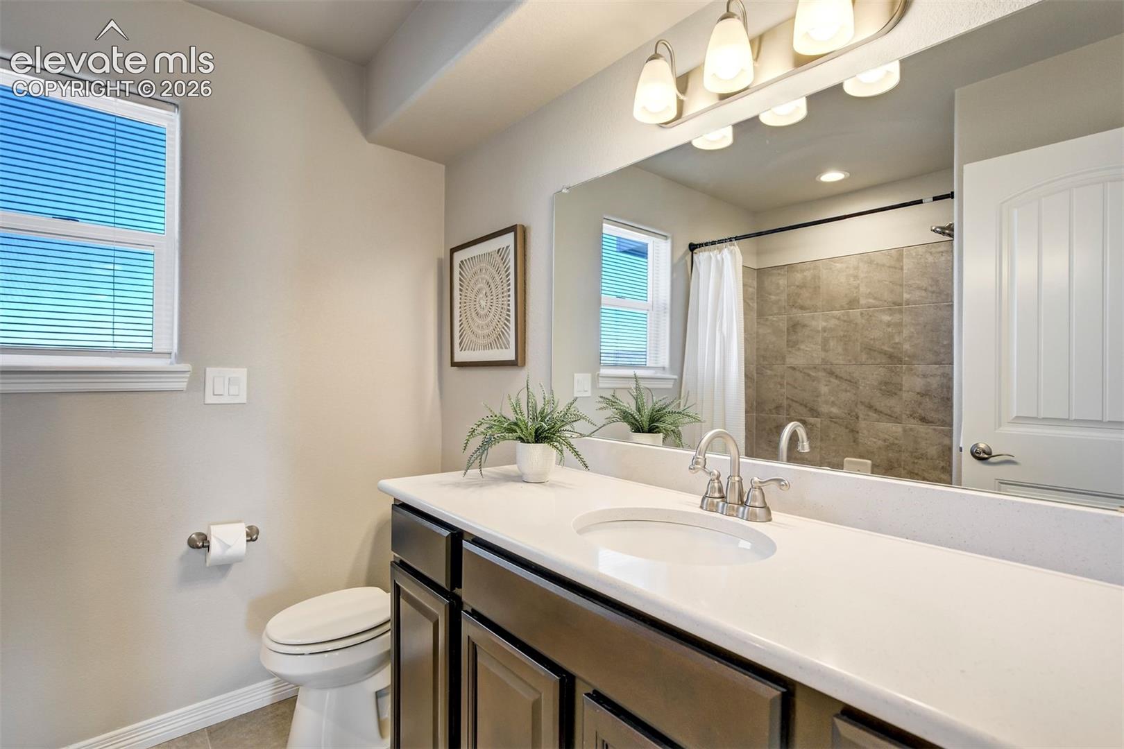 Bathroom featuring a single vanity with a white countertop, an undermount sink, a shower with a tiled surround, and a window with blinds