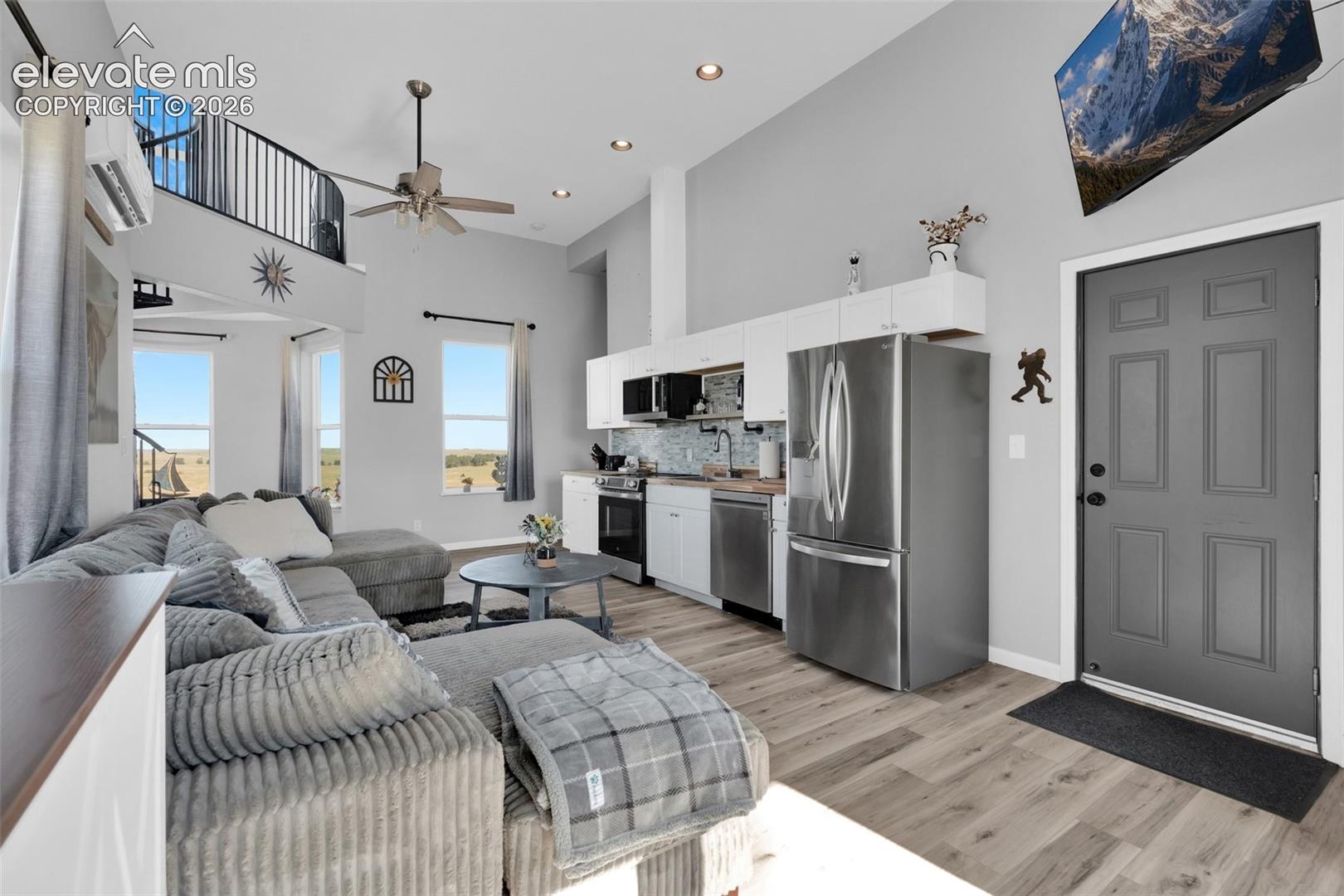 Vaulted ceilings featuring recessed lighting, a mezzanine level with iron railing, wood-finish flooring, white cabinetry, and stainless steel appliances