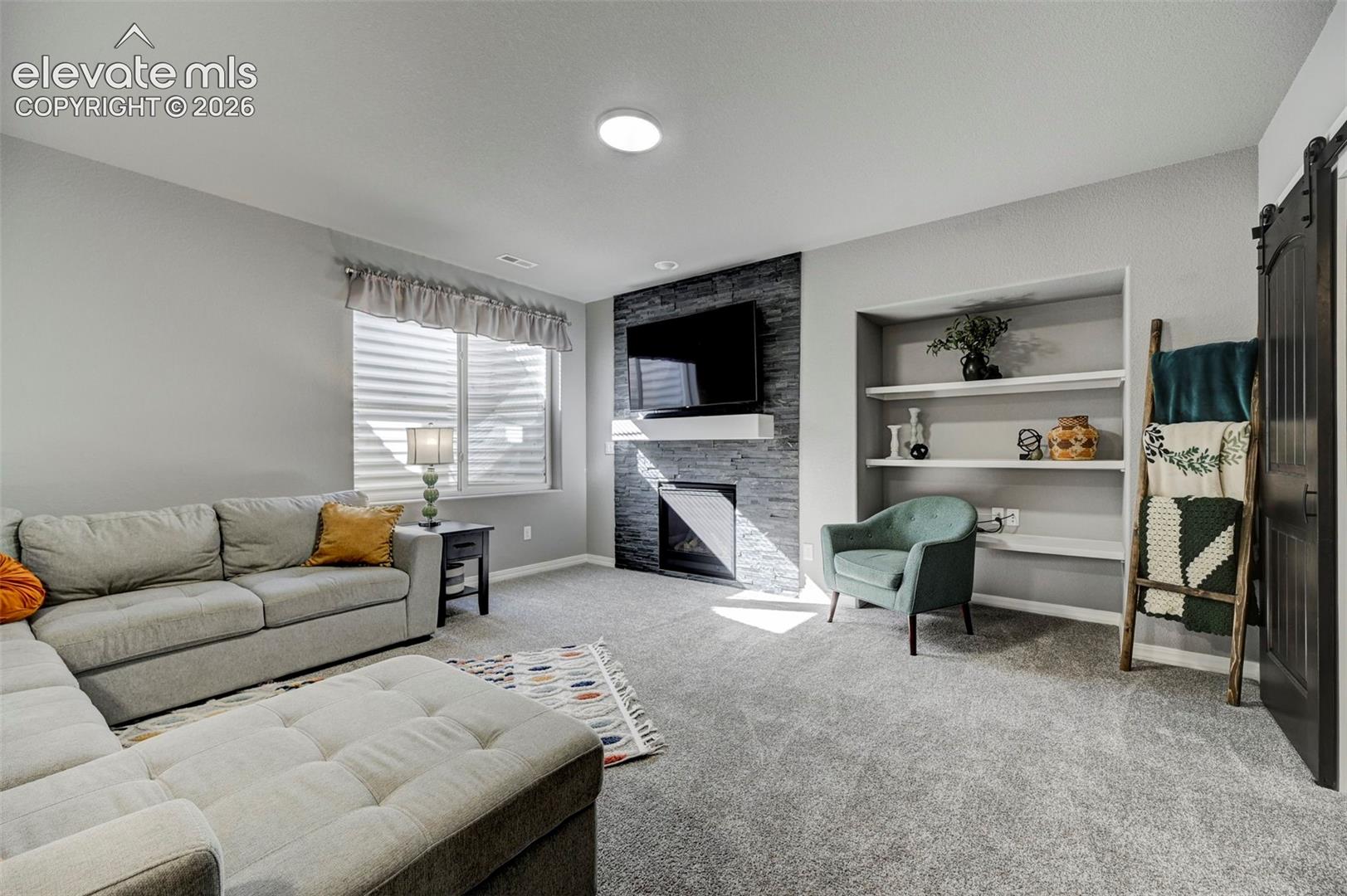 Living area featuring a stone-clad fireplace with a white mantel, recessed shelving, and light gray wall-to-wall carpeting