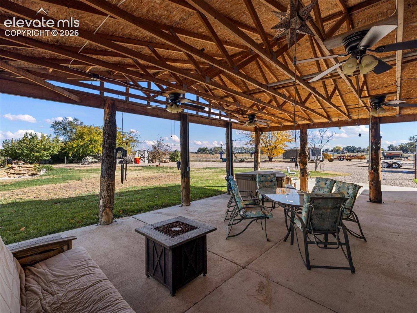 Covered patio featuring a concrete floor, rustic timber support columns, and exposed wood-truss ceiling with integrated ceiling fans