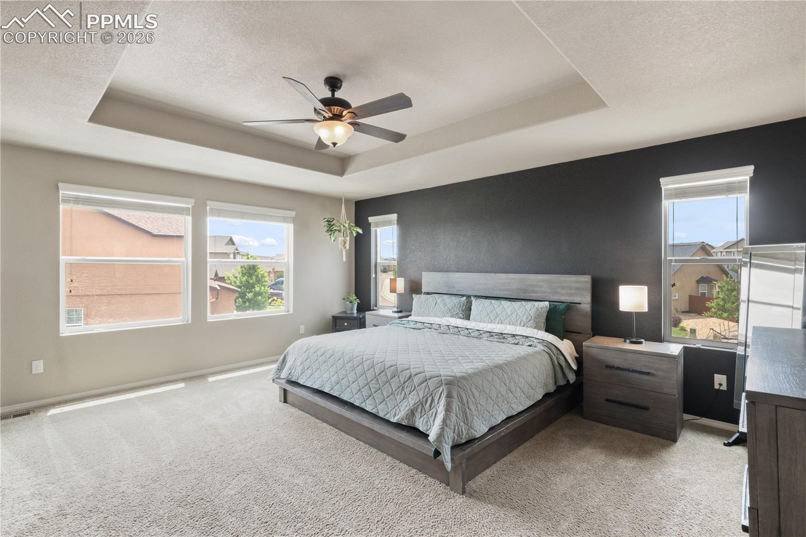 Bedroom featuring light carpet, ceiling fan, a textured ceiling, and a tray ceiling