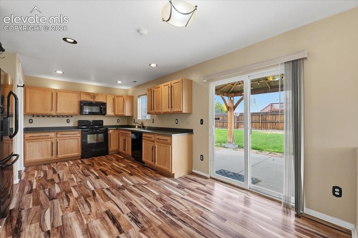 Kitchen featuring wood-finish flooring, light wood cabinetry, black appliances, recessed lighting, and a sliding glass door