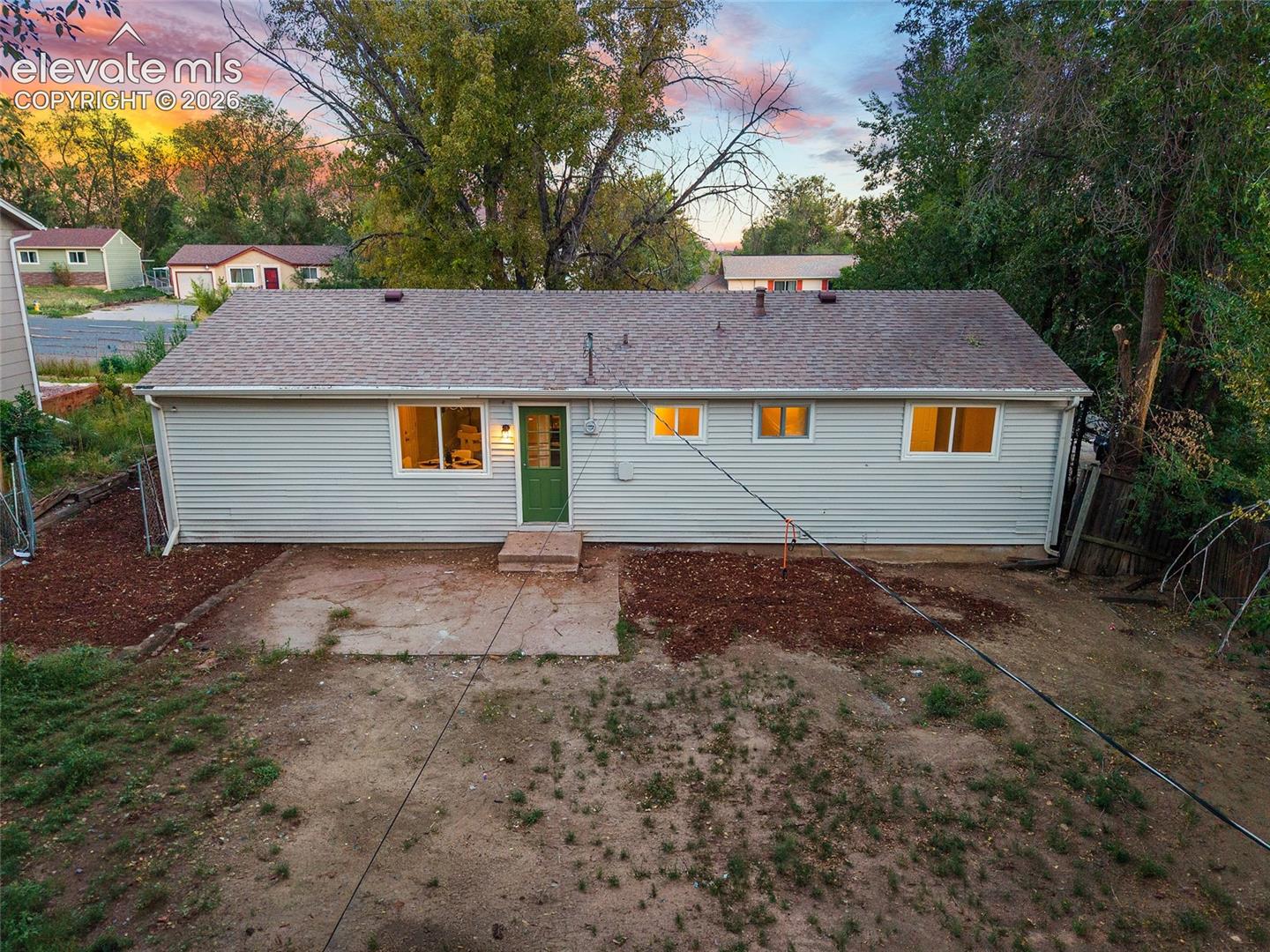 Light-colored horizontal siding, asphalt shingle roof, green rear entry door, and a concrete patio pad