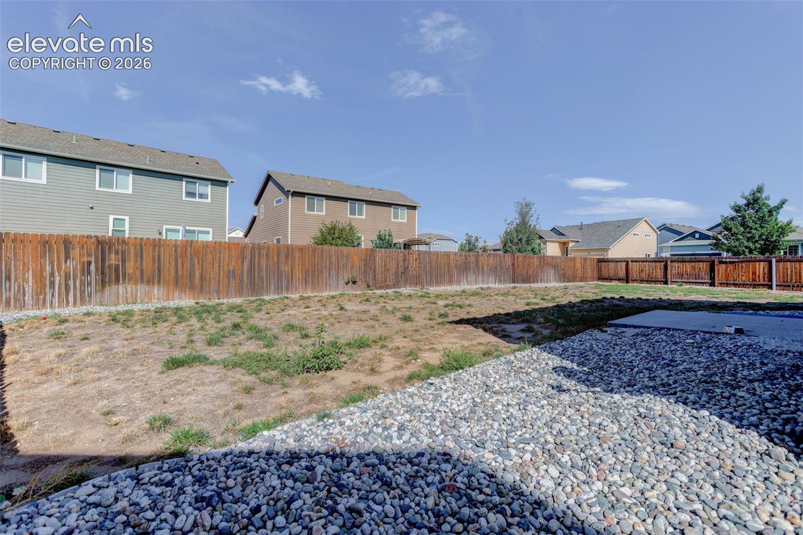 Expansive outdoor space featuring a wood fence, gravel landscaping, and a concrete pad