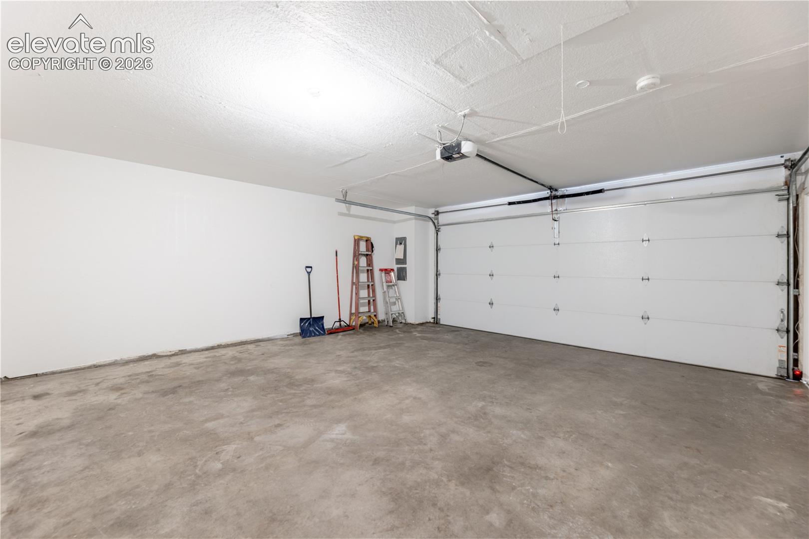 Spacious two-car garage featuring a concrete floor, high ceilings, and an automated overhead door opener