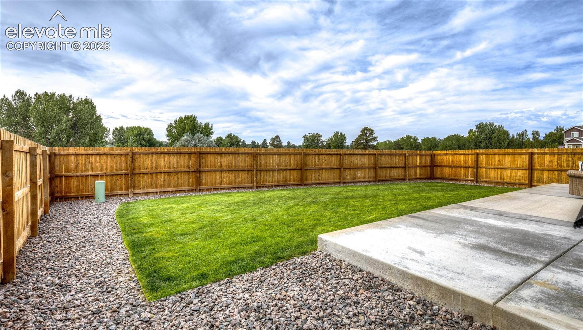Rear yard featuring a full-perimeter wood privacy fence, a manicured lawn, a concrete patio, and decorative gravel landscaping