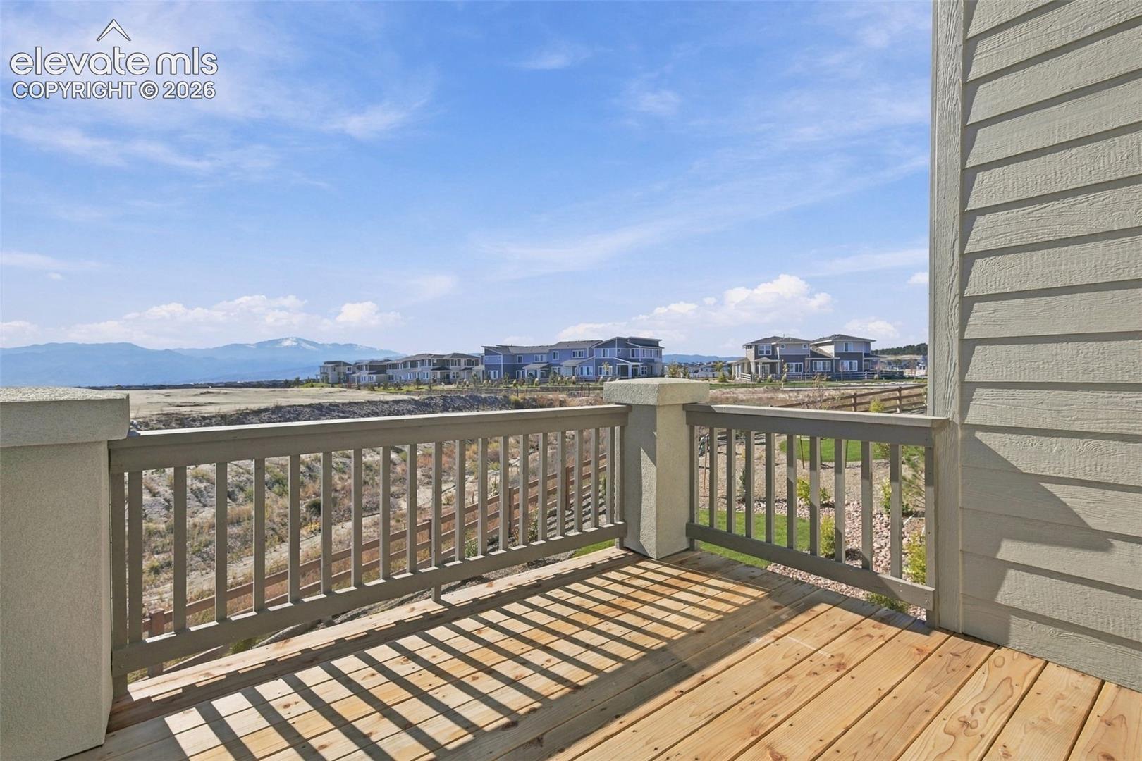Deck with wood plank flooring and a slatted railing, featuring a distant mountain backdrop and visible residential structures