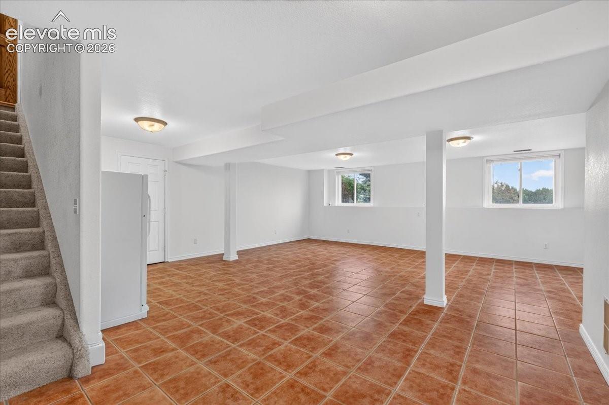 Open-concept room featuring terra-cotta tile flooring, flush-mount ceiling lighting, natural light through double-pane windows, and a carpeted staircase