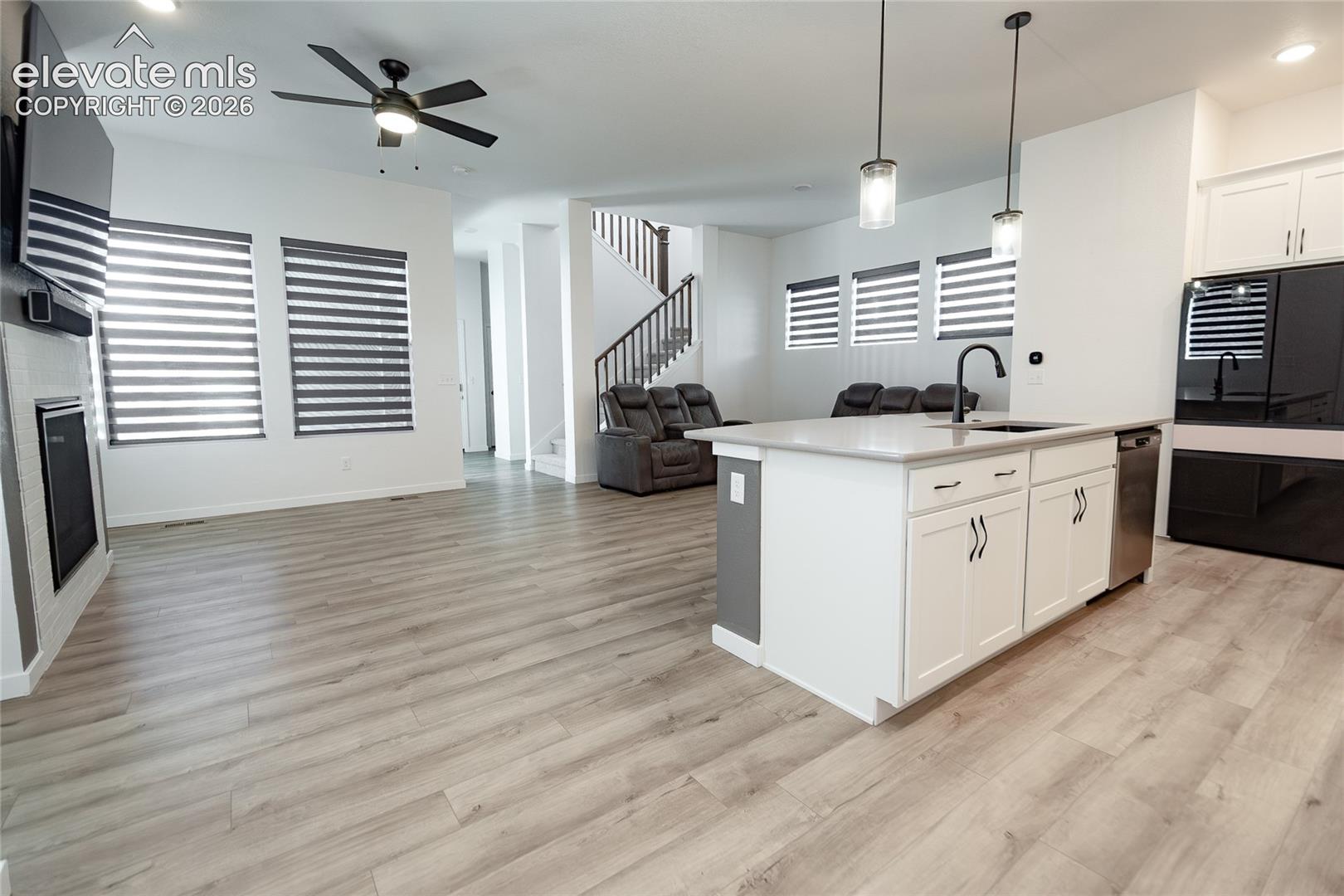 Open concept living area featuring wood-finish flooring, a kitchen island with stone countertops, a modern fireplace, ceiling-mounted lighting, and a staircase with a wooden railing