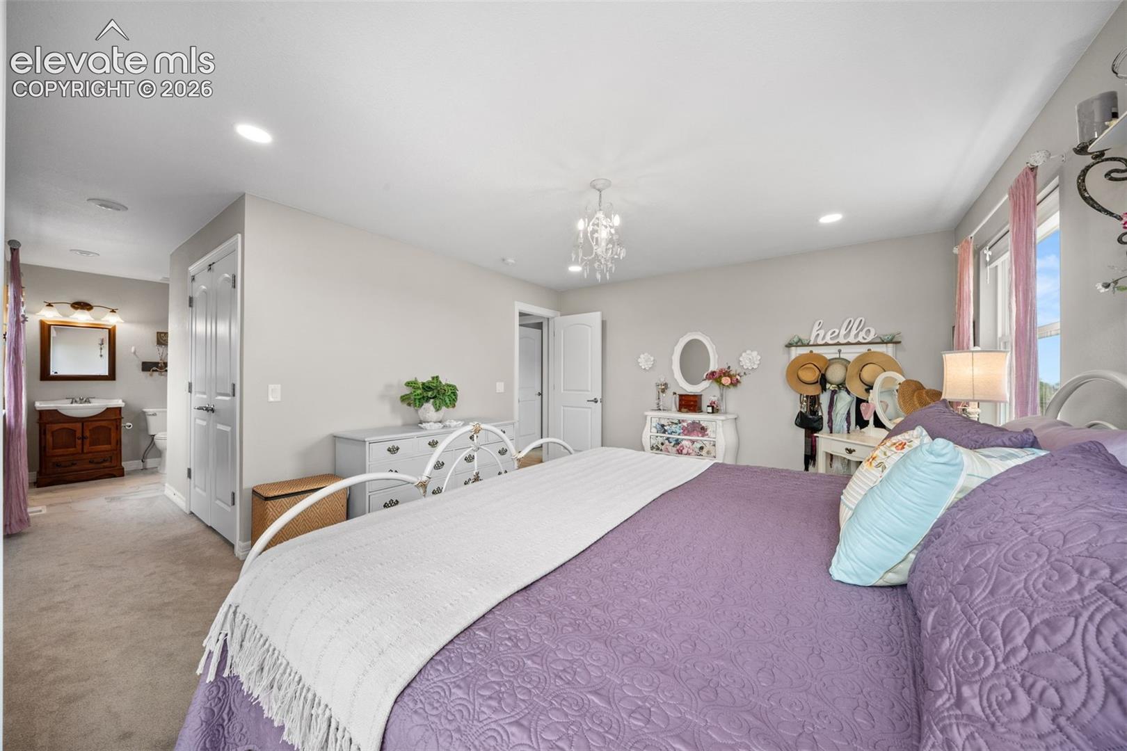 Spacious bedroom featuring light neutral wall tones, recessed lighting, and a crystal chandelier