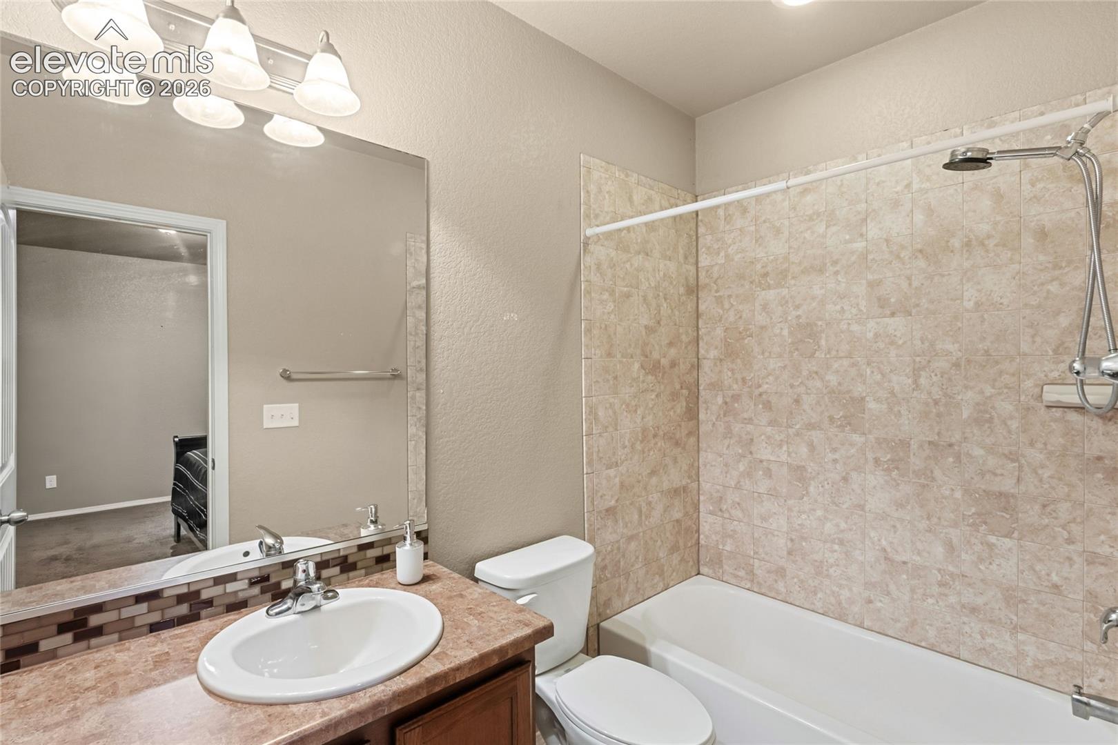 Bathroom featuring a vanity with an integrated basin, a multi-tone mosaic tile backsplash, a full-width mirror, and a shower-tub combination with tiled surround