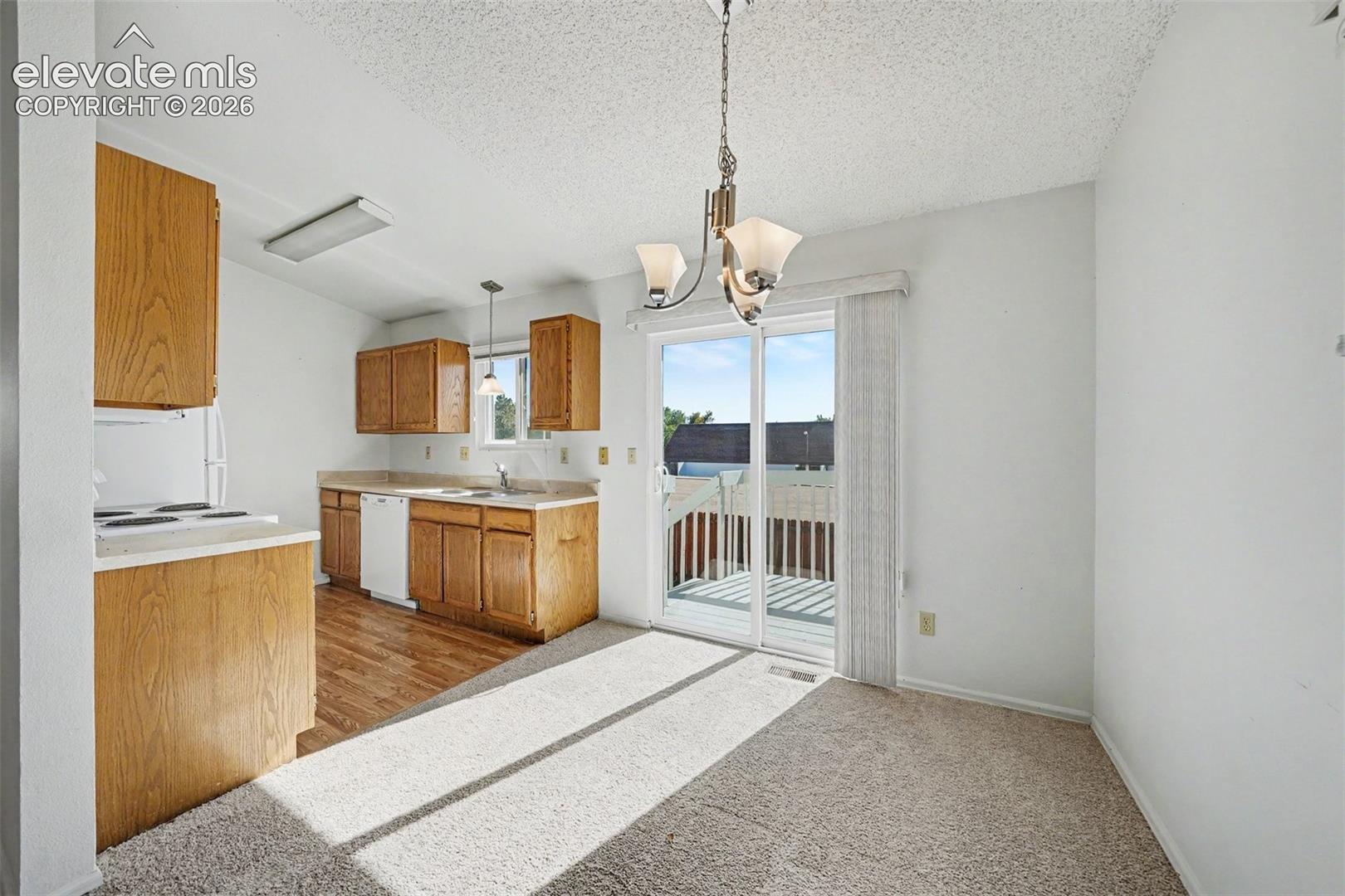 Kitchen featuring wood-finish cabinetry, solid surface countertops, and wood-finish flooring, complemented by a hanging chandelier and sliding glass doors leading to an exterior deck
