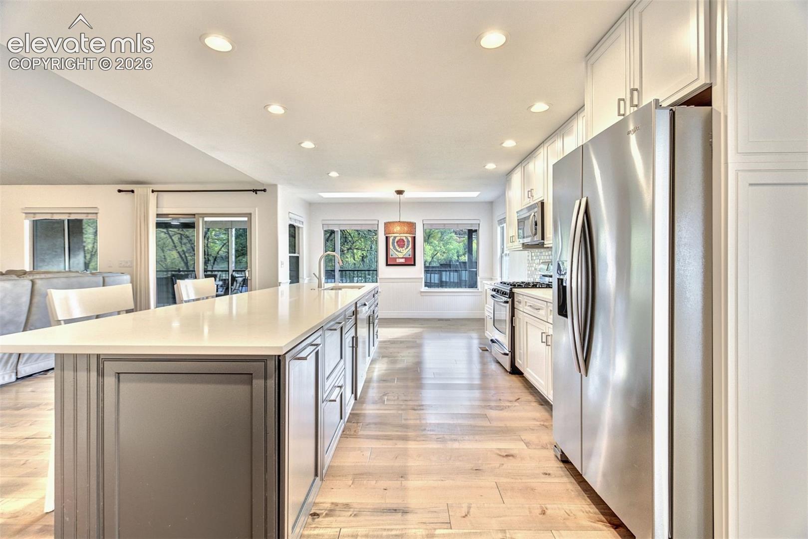 Kitchen featuring a central island with stone-style countertops, shaker-style cabinetry, stainless steel appliances, and wood-finish flooring