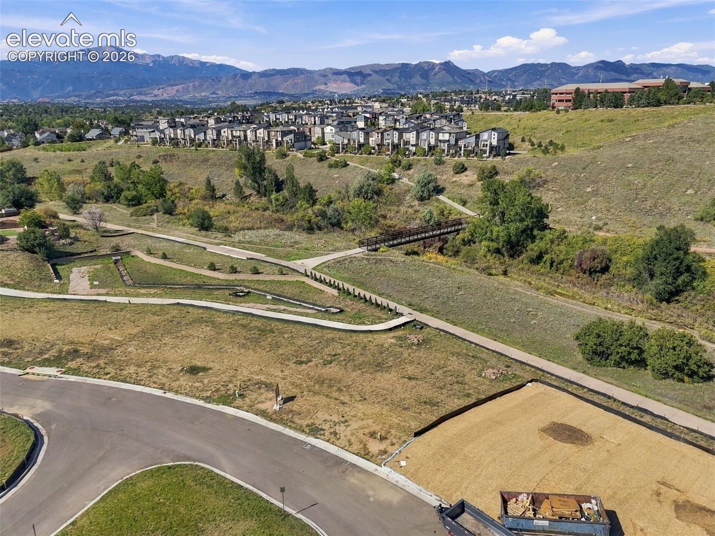 Mountain backdrop, residential structures, open space, paved walking paths, and a pedestrian bridge