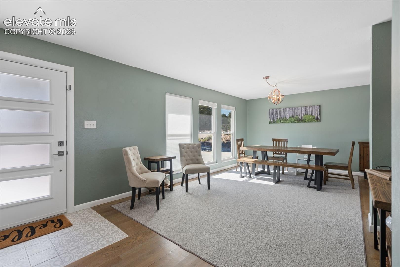 Front entry featuring a four-panel door with frosted glass inserts, wood-finish flooring, patterned tile entryway, triple-pane windows, and a metal orb chandelier