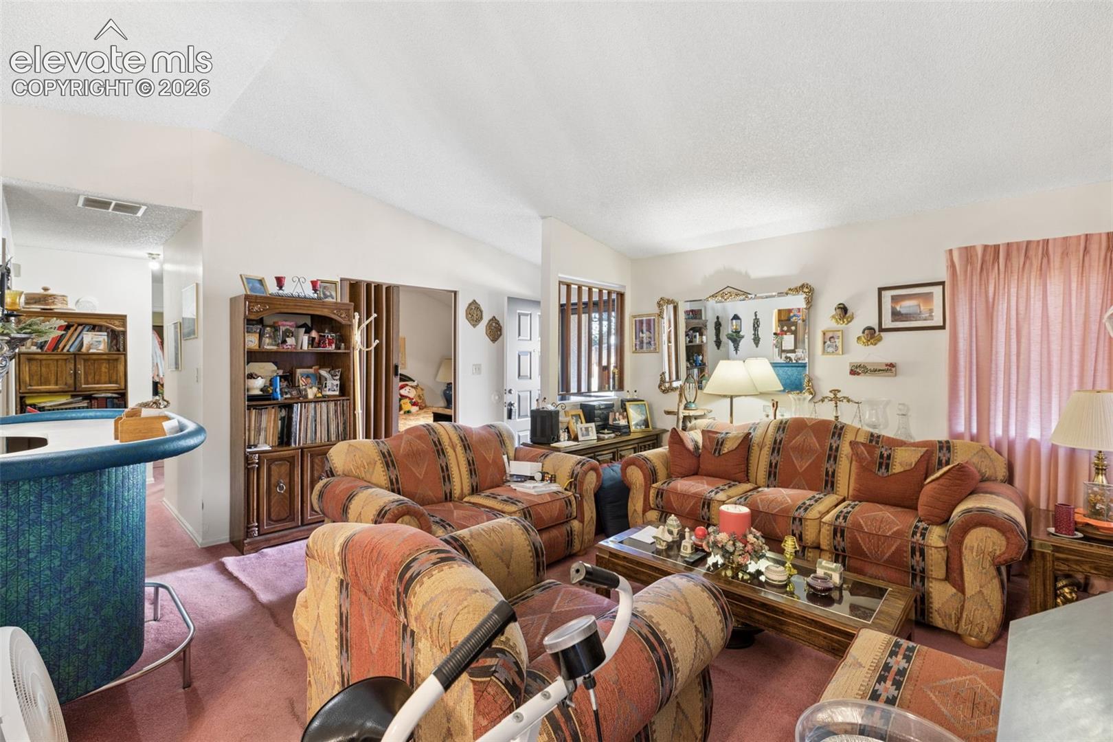 Living area featuring vaulted ceilings, a built-in wet bar with a blue countertop, and decorative wall mirror
