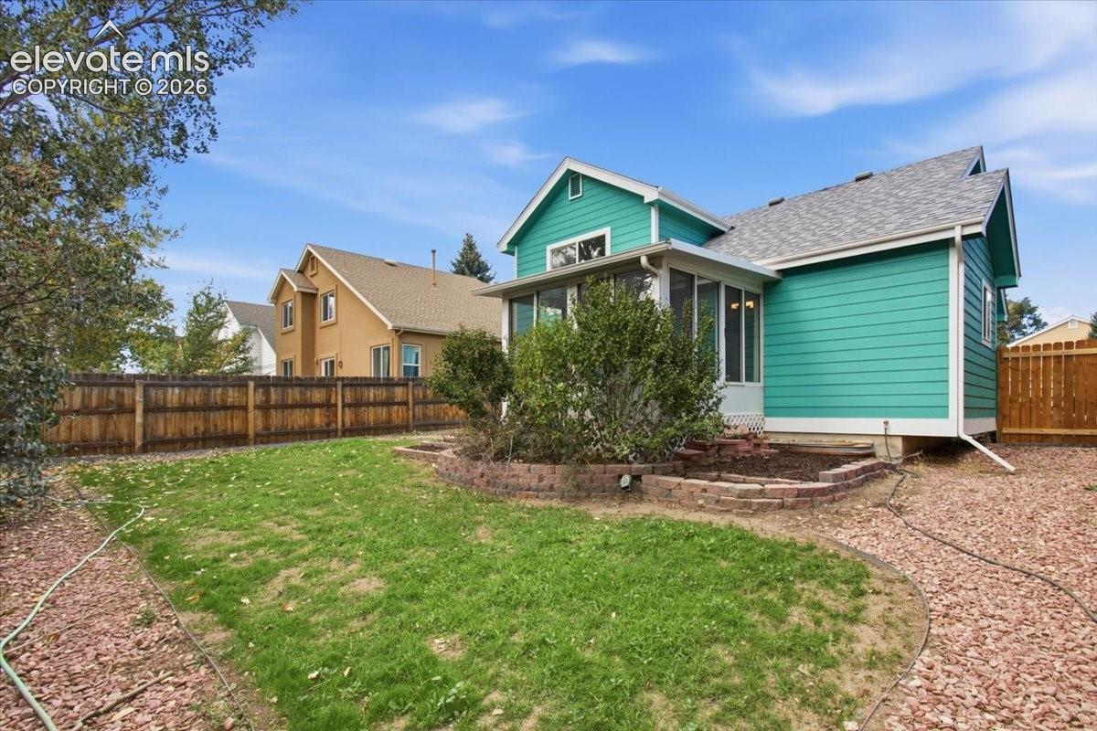 Exterior featuring turquoise horizontal siding, a screened-in porch, a stone-block raised garden bed, and a wooden privacy fence