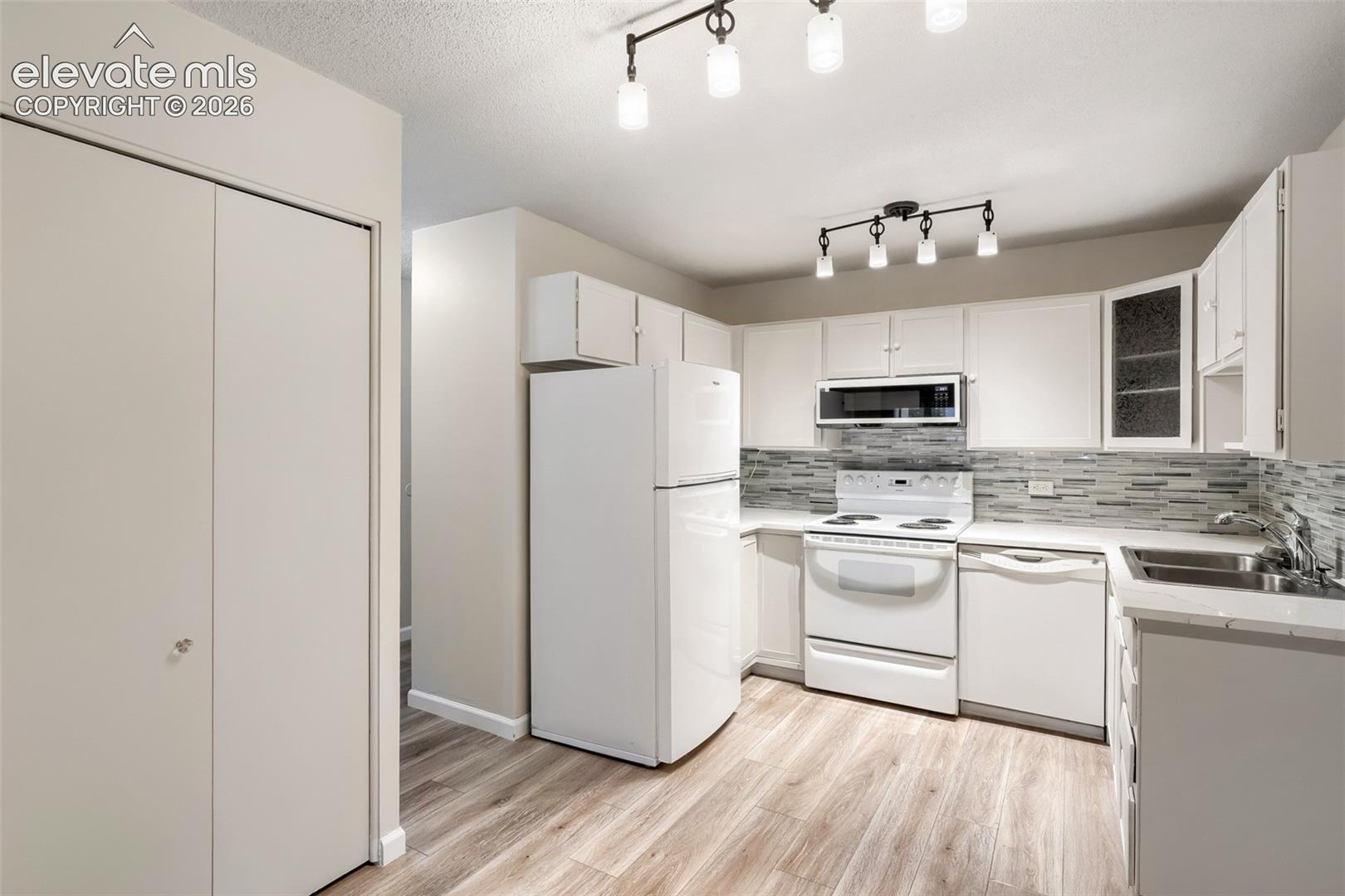 Kitchen featuring wood-finish flooring, white cabinetry, and a mosaic tile backsplash