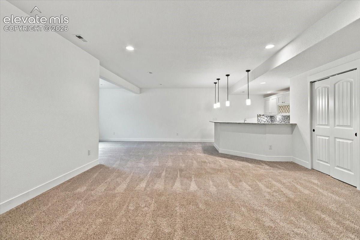 Open-concept interior featuring carpeted flooring, a peninsula with stone-finish countertops, three suspended pendant lights, recessed ceiling lighting, and double-panel doors