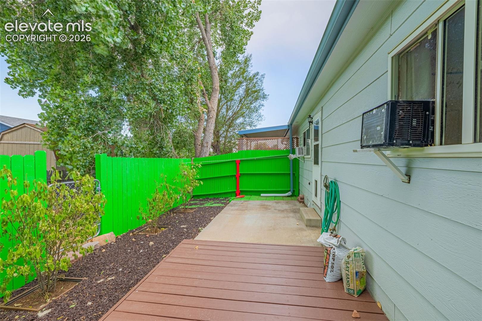 Backyard featuring a wood deck, concrete patio, and a vibrant green privacy fence