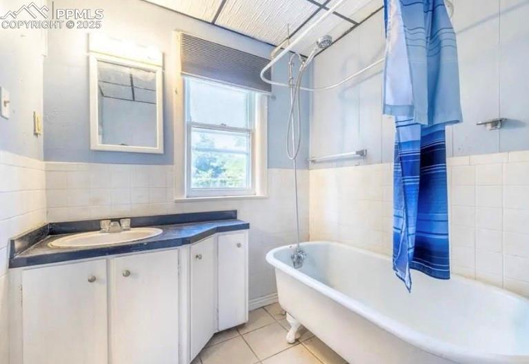 Full bath with tile walls, a wainscoted wall, vanity, tile patterned floors, and shower / bath combo with shower curtain