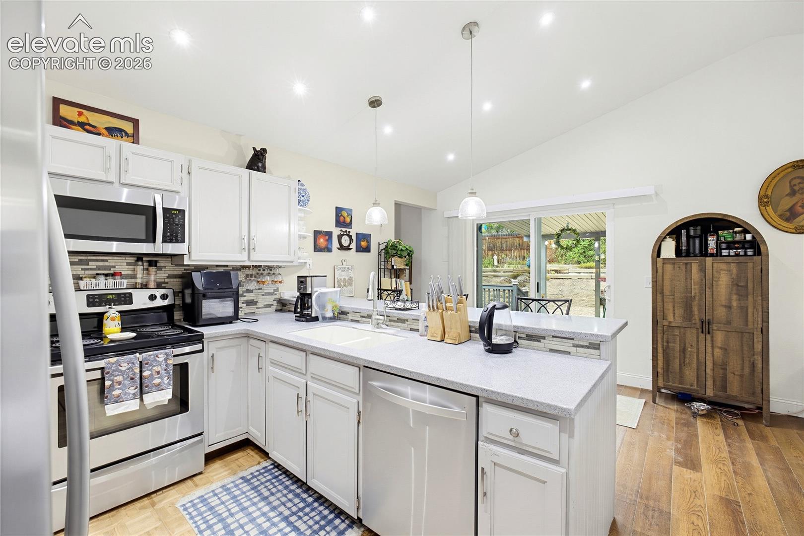 Kitchen with vaulted ceiling, recessed lighting, white cabinetry, integrated stainless steel appliances, and wood-finish flooring