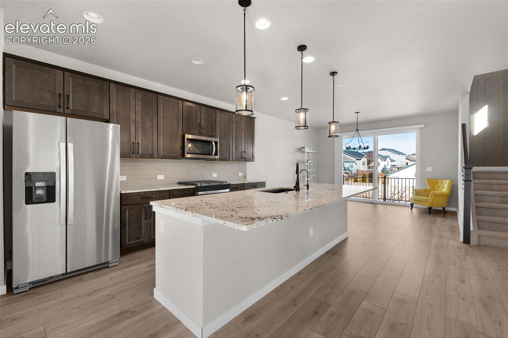 Kitchen featuring stainless steel appliances, dark wood cabinetry, a large island with a light-toned countertop, and wood-finish flooring
