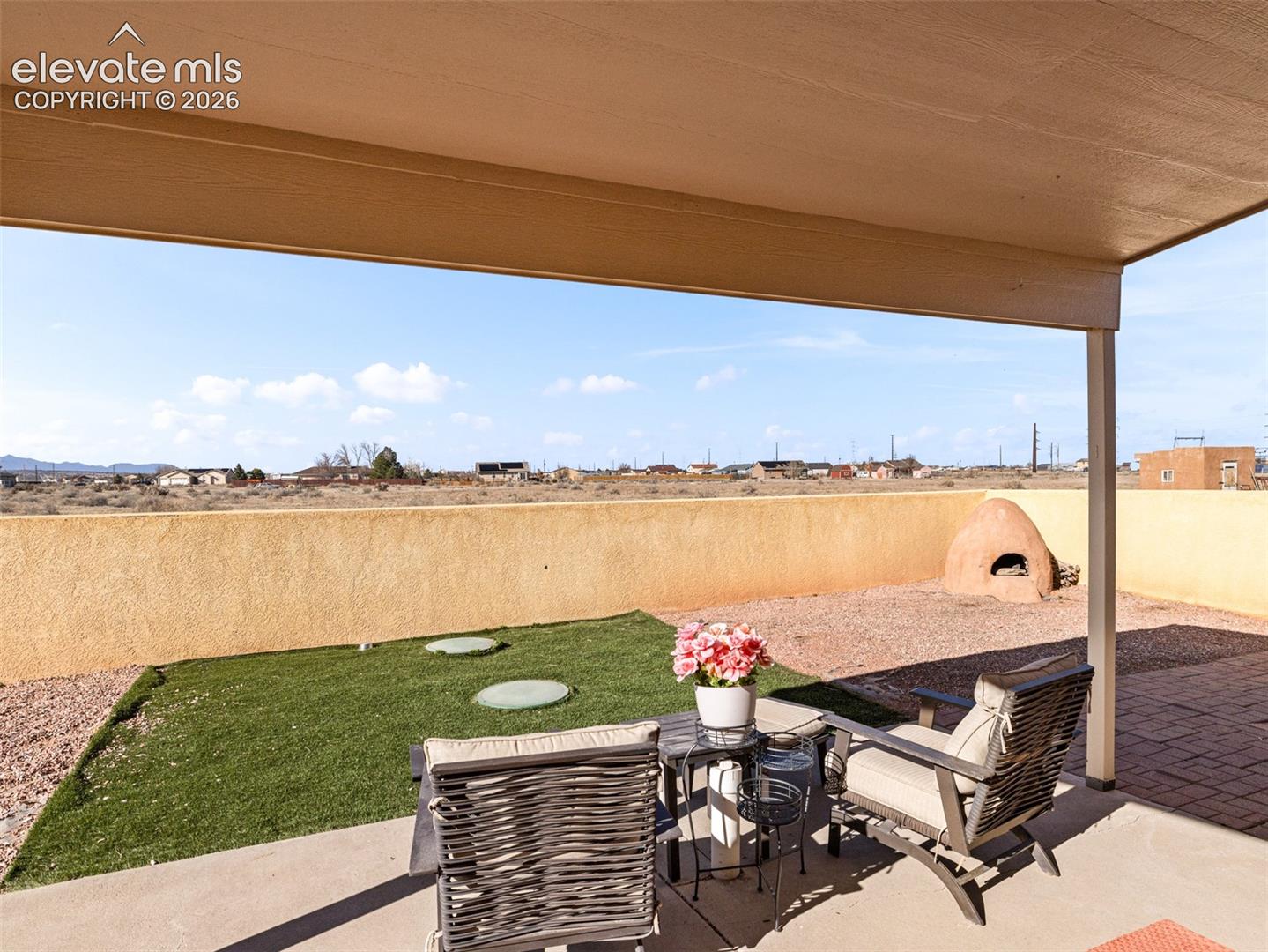 Covered patio with concrete flooring, stucco wall, artificial turf area, and built-in outdoor oven