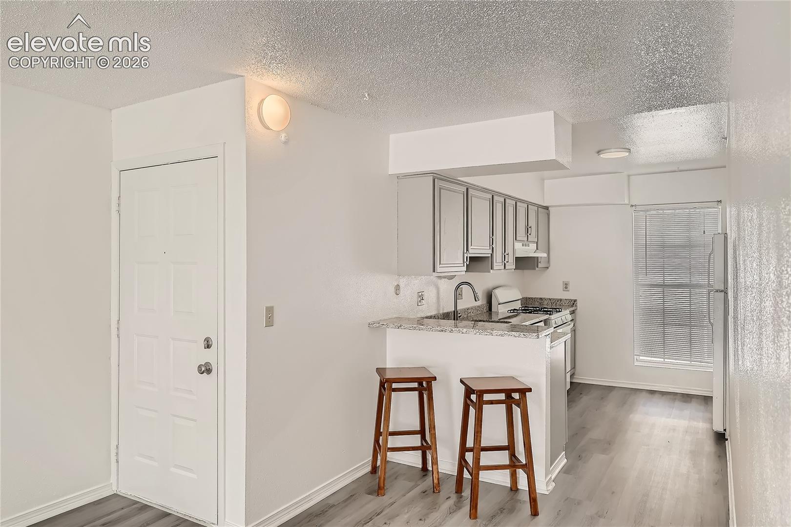 Kitchen featuring light gray shaker-style cabinetry, stone-finish countertops, wood-finish flooring, and a breakfast bar