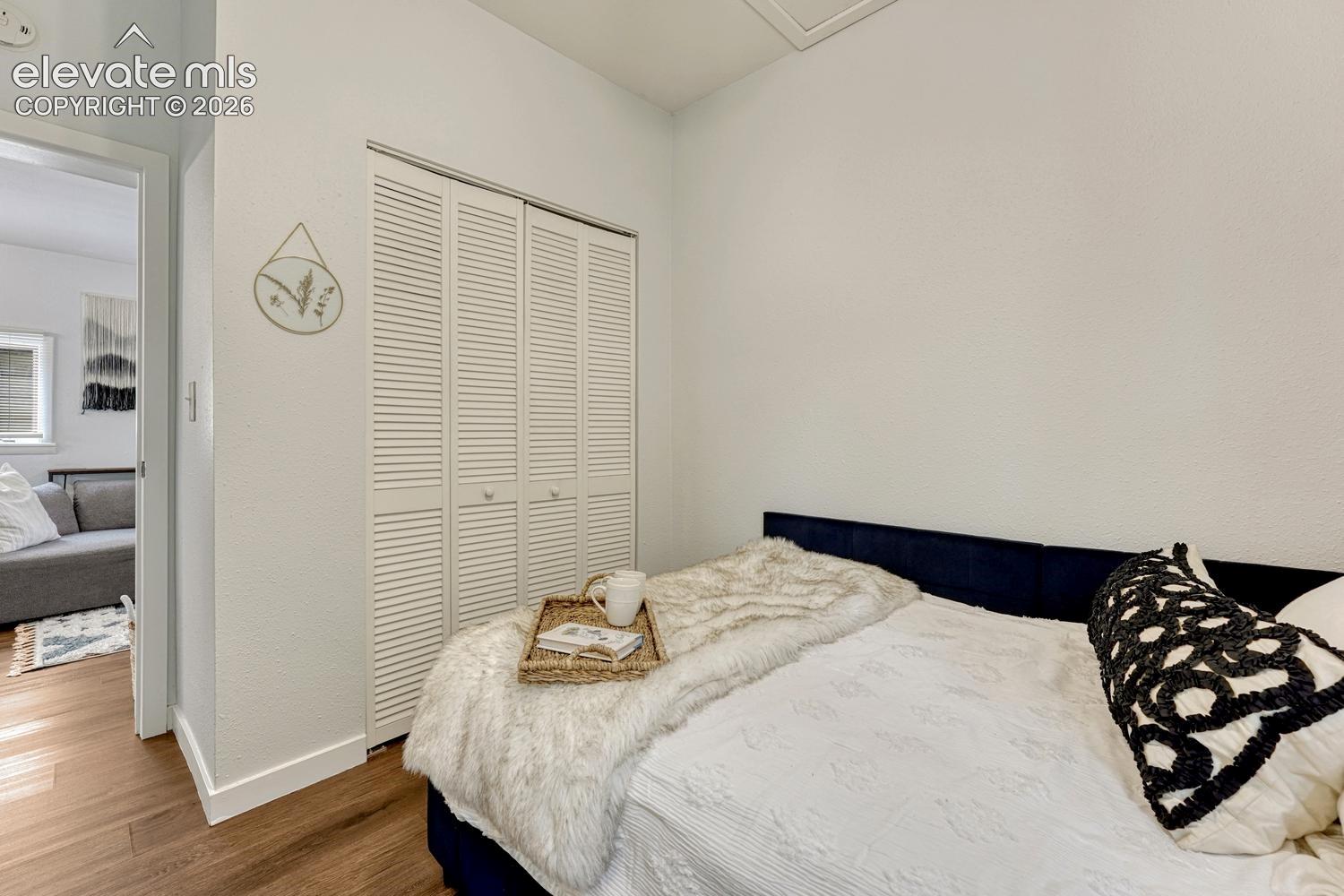Wood-finish flooring, white louvered bifold closet doors, and white painted walls
