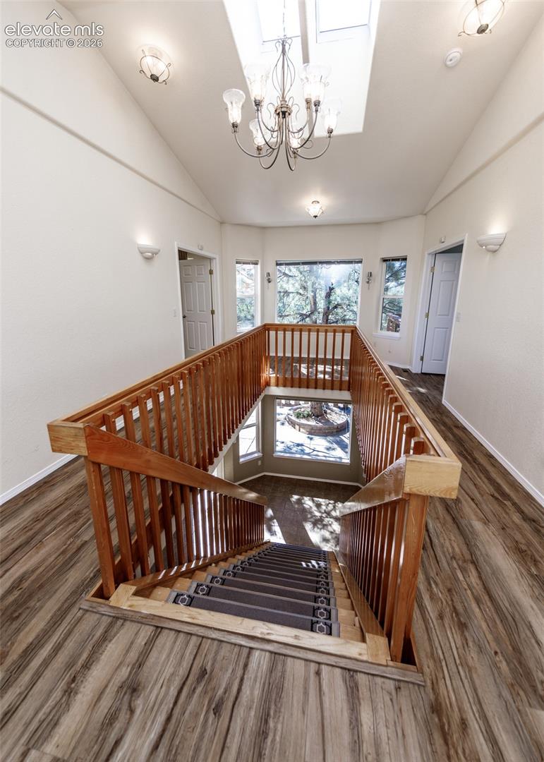Vaulted ceilings featuring a skylight, wood-finish flooring, wood railing, chandelier, and wall-mounted sconces