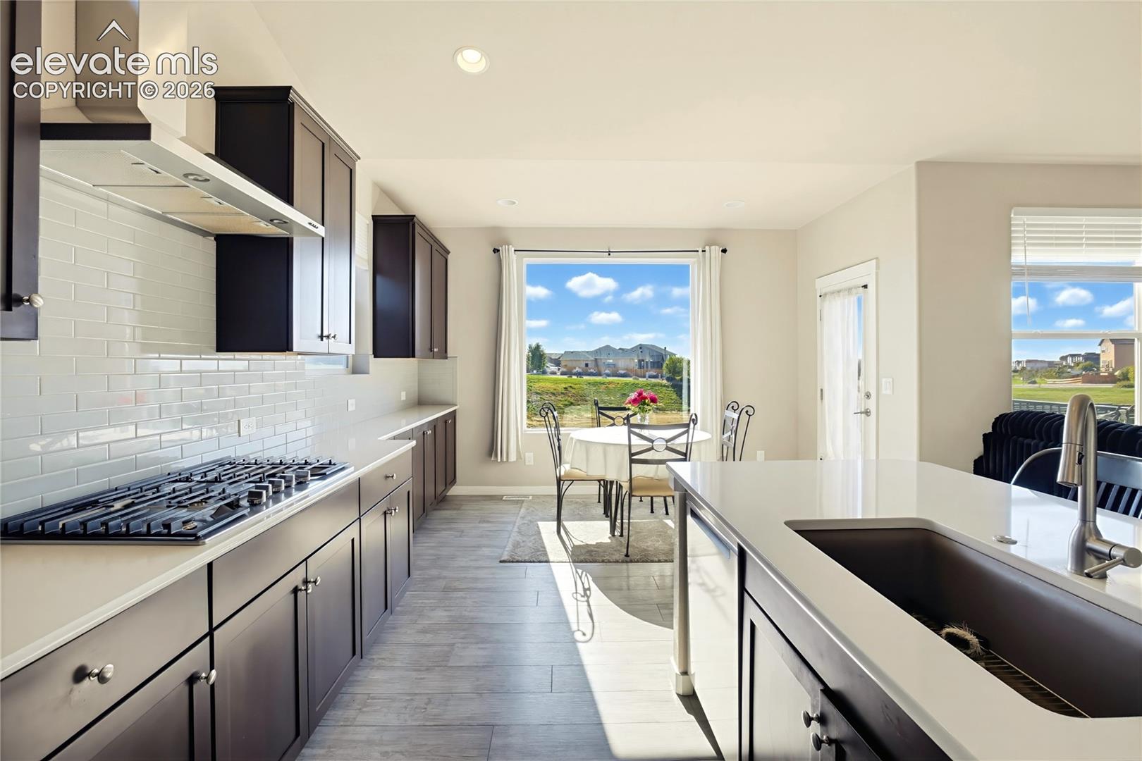 Kitchen featuring dark cabinetry, expansive stone-surface countertops, subway tile backsplash, stainless steel gas cooktop with range hood, and tile flooring