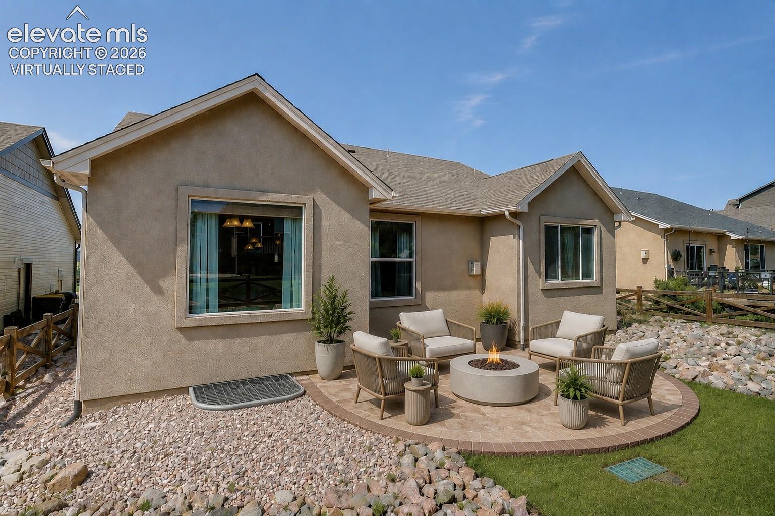 Virtually Staged - Stucco exterior with a gable roofline, featuring an exterior patio with a built-in fire pit, surrounded by a landscaped rock and grass area
