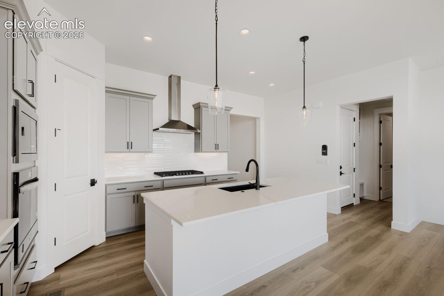 Contemporary kitchen featuring an integrated oven and microwave, a center island with sink, pendant lighting, shaker-style cabinetry, and wood-finish flooring
