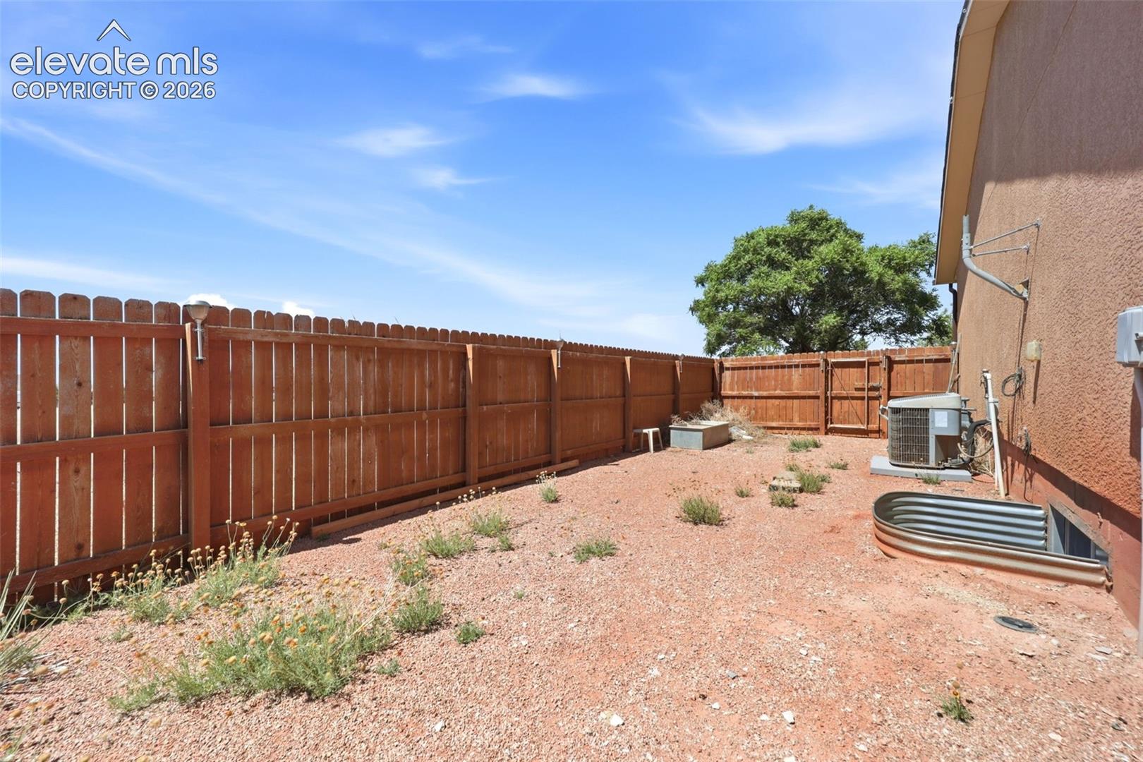 Enclosed backyard space featuring a wood privacy fence and a stucco exterior wall