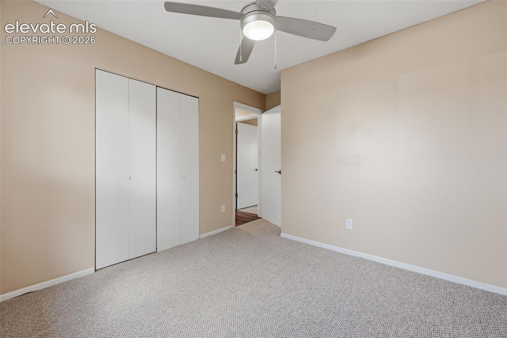 Neutral tone wall paint, textured carpeting, bi-fold closet doors, and a ceiling fan with integrated lighting