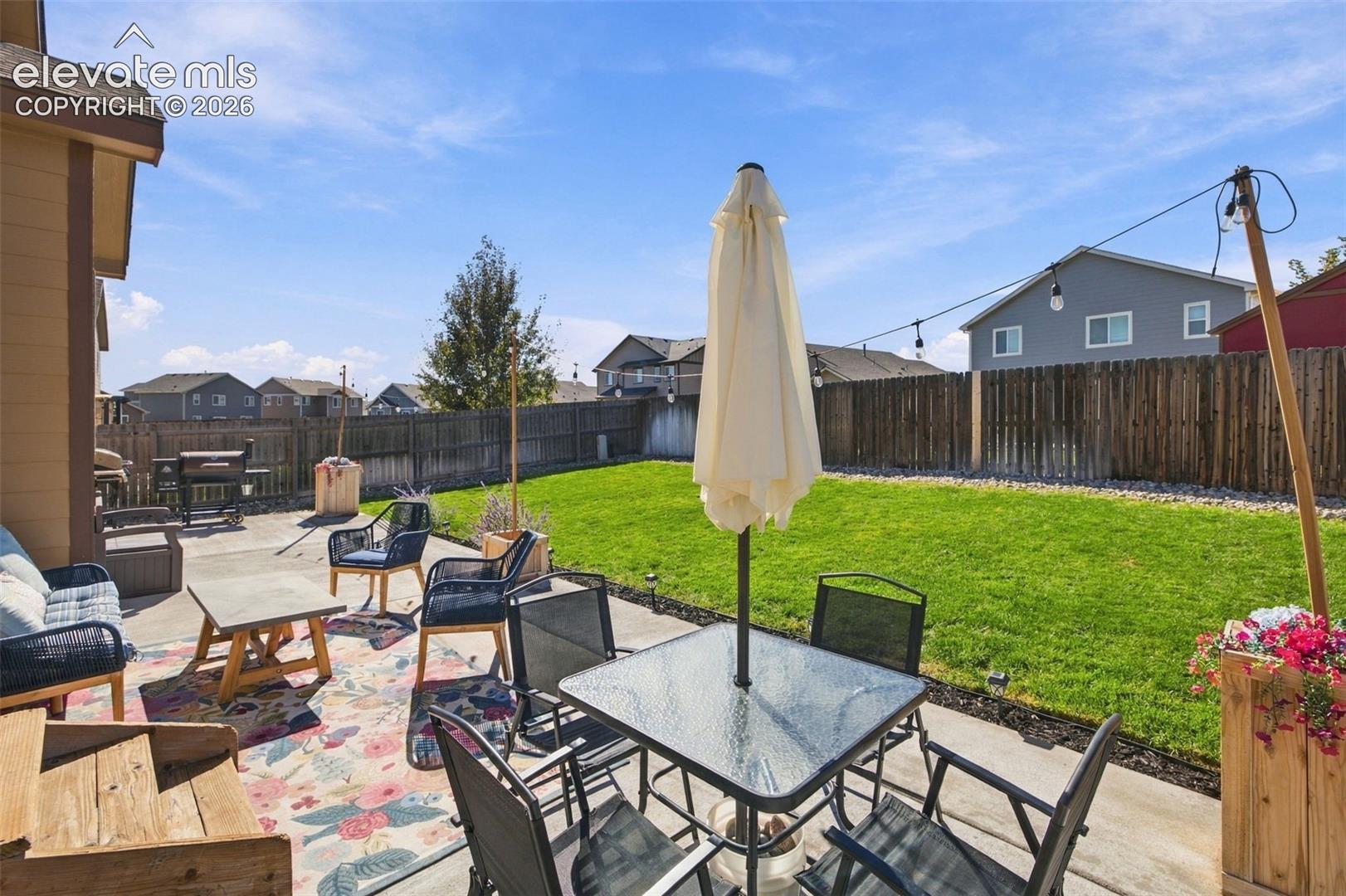 Rear concrete patio featuring a manicured lawn, perimeter wood privacy fencing, and overhead string lighting