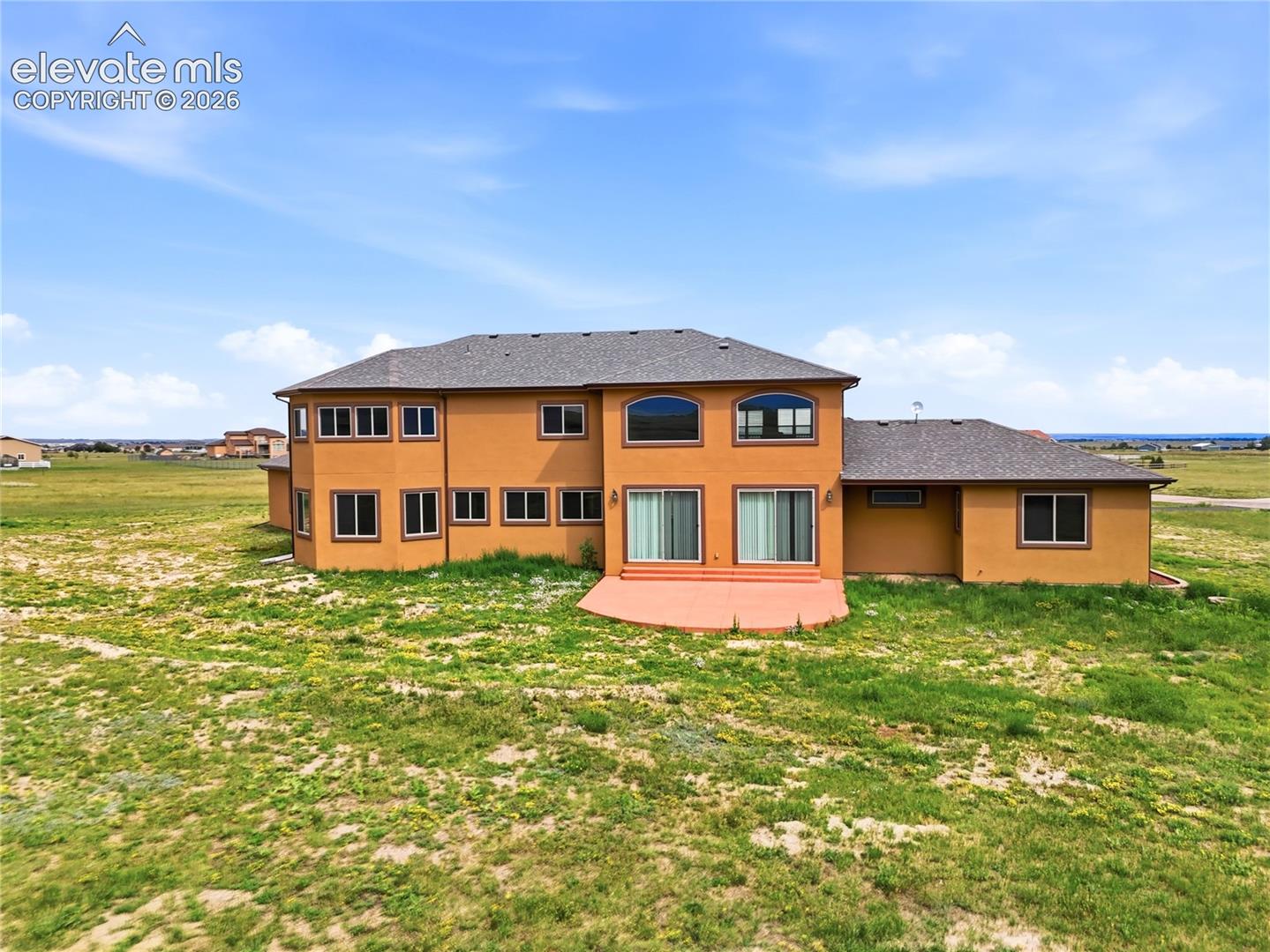 Two-story stucco exterior with multiple windows, arched windows, and a paved patio