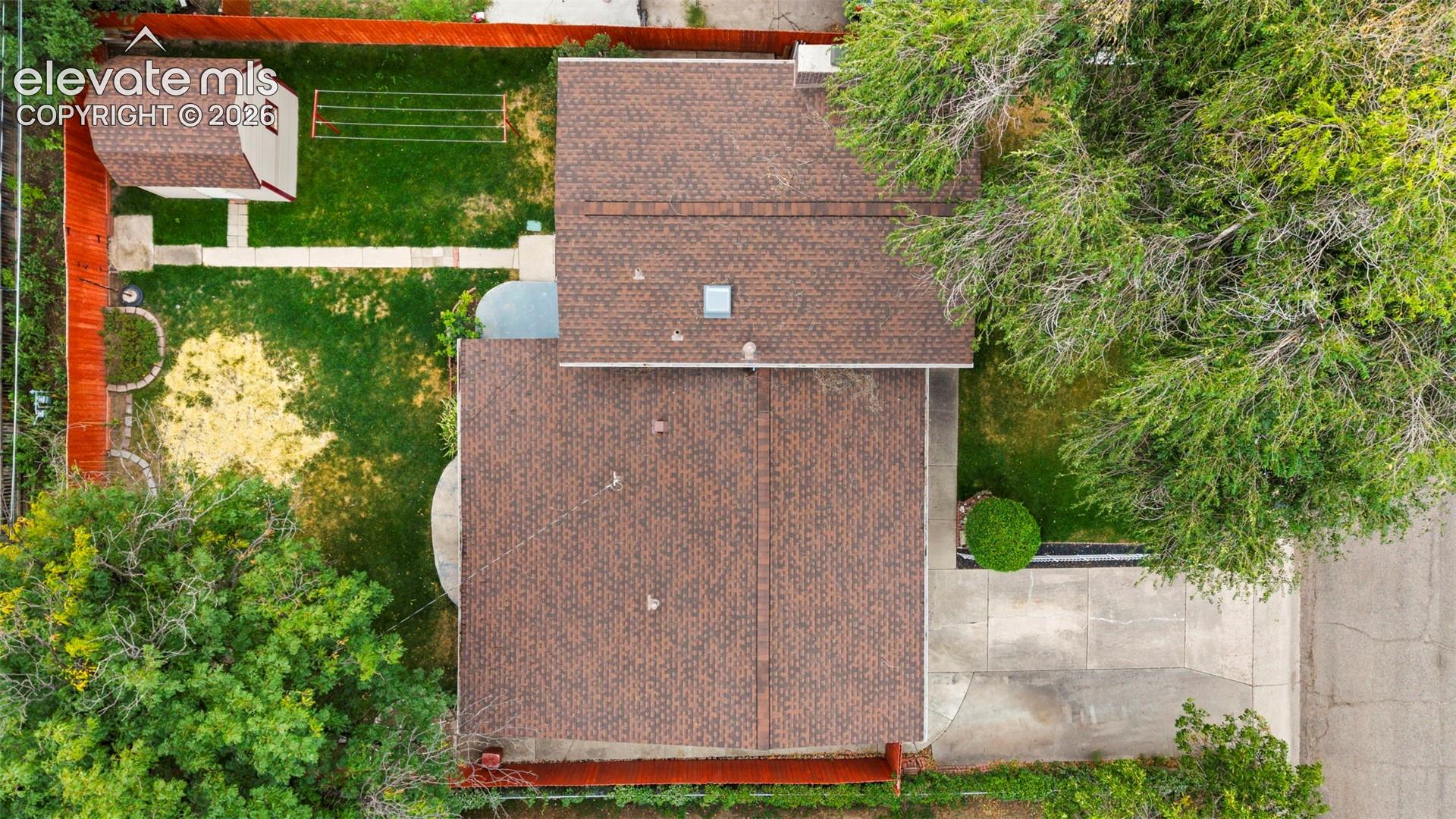 Brown shingle roof with skylight, detached storage shed, privacy fencing, and green lawn