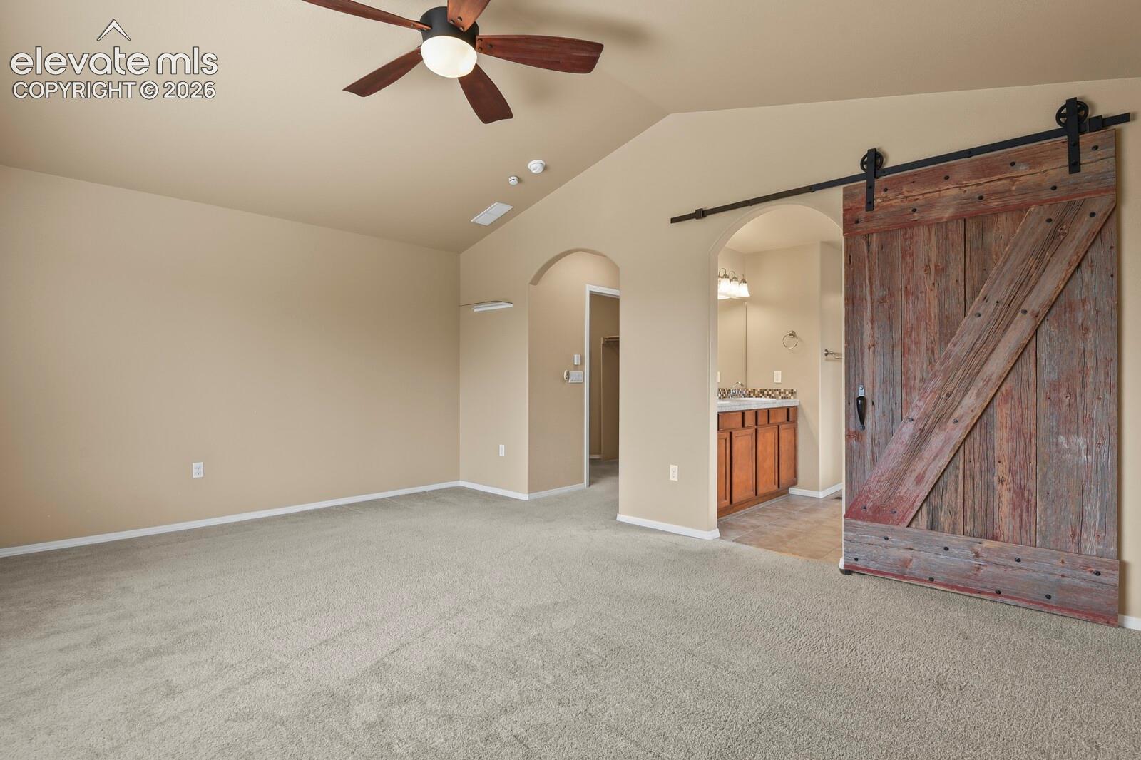 Vaulted ceiling with a ceiling fan, carpeted flooring, and a rustic wood sliding barn door