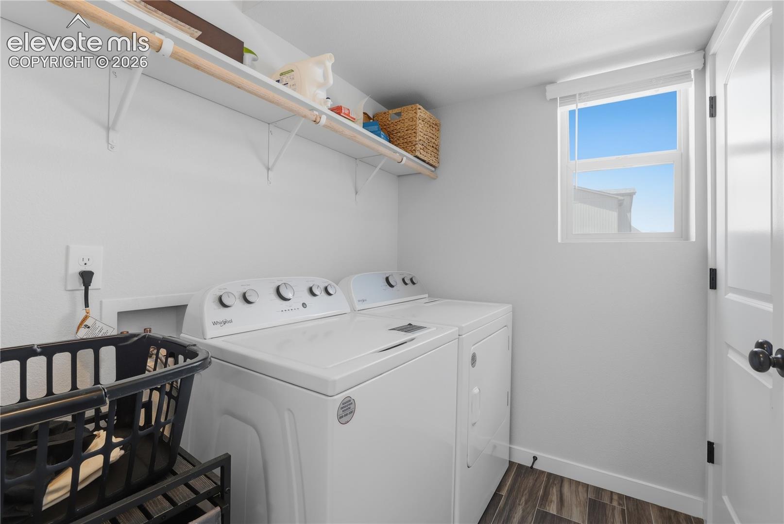 Dedicated laundry space featuring wood-finish flooring, white walls, and a white window with a privacy blind
