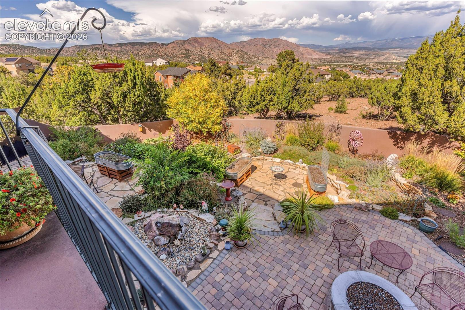 Landscaped backyard featuring flagstone hardscaping, multi-colored paver patio, stone-lined rock garden, and perimeter privacy wall with mountainous backdrop
