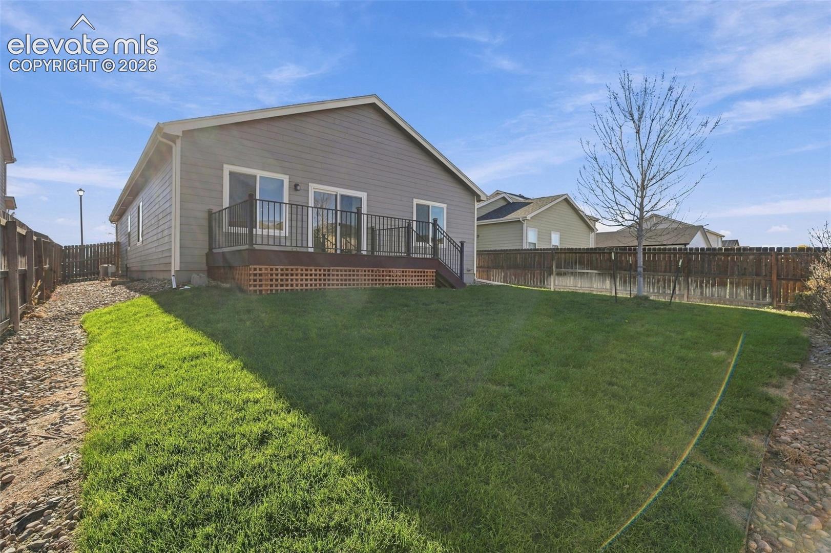 Rear exterior featuring horizontal lap siding, an elevated wood deck with metal railings, and a fenced-in yard with a lawn and rock landscaping borders