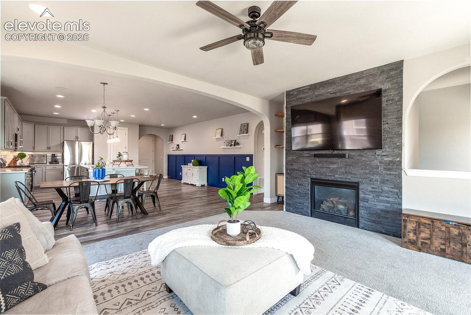 Open-concept living space, archway details, stone front gas fireplace, wall mounted TV