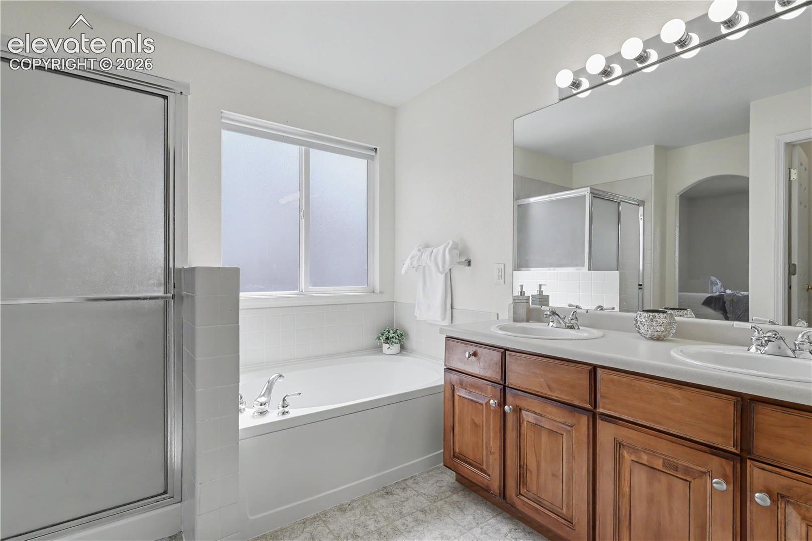 Bathroom featuring a double vanity with wood cabinetry and dual sinks, a large mirror, a built-in bathtub, and a shower with a sliding glass door