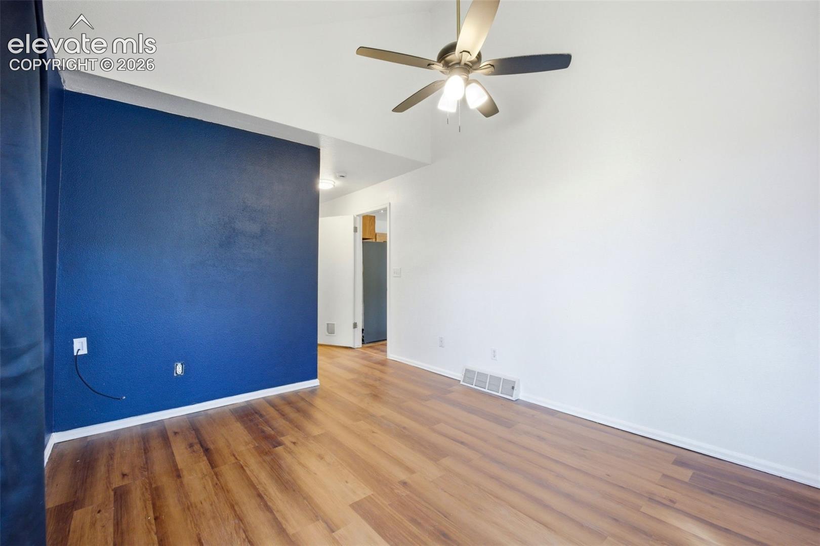 Room featuring vaulted ceilings, wood-finish flooring, a dark blue accent wall, and a multi-light ceiling fan