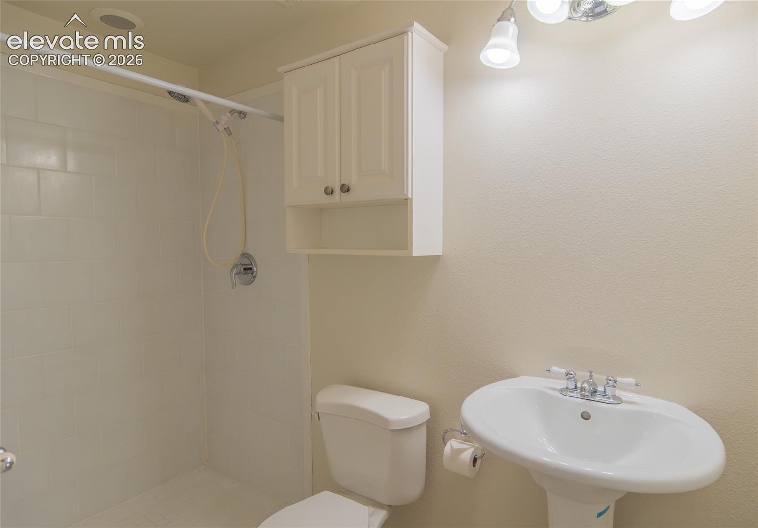 Convenient three-quarter bath with a tiled shower, handheld showerhead, and pedestal sink.